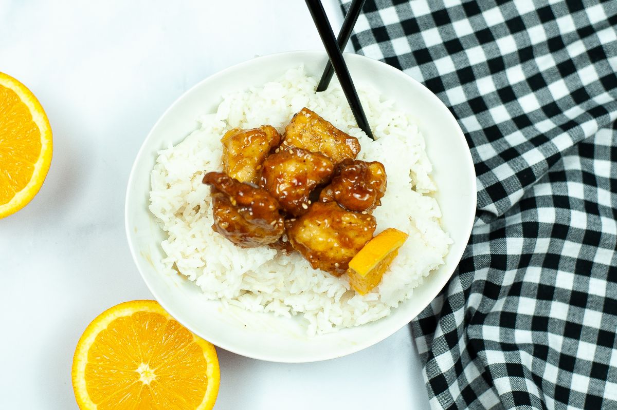Air Fryer Copycat Panda Express Orange Chicken in a white bowl with rice and chopsticks.
