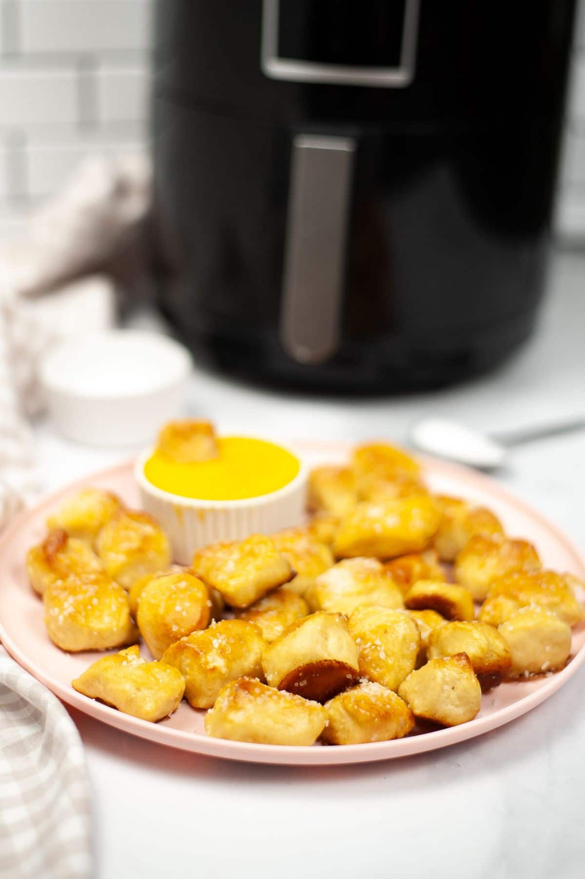 Air Fryer Pretzel Bites on a pink plate with dipping sauce on the side and an air fryer blurred in the background