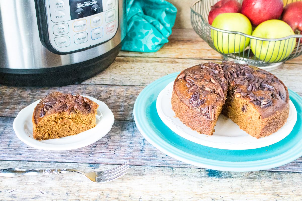 a slice of Instant Pot Applesauce Cake on a white plate with an instant pot and more cake on a plate next to it