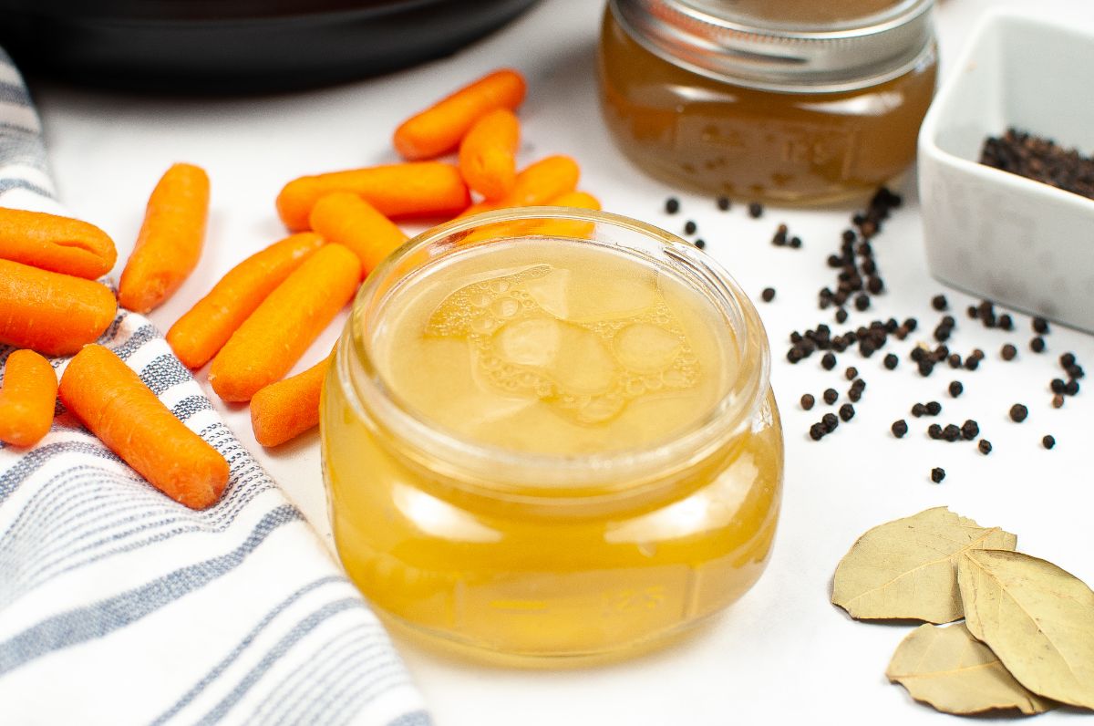 Instant Pot Chicken Bone Broth in a jar next to carrots, peppercorns and bay leaves