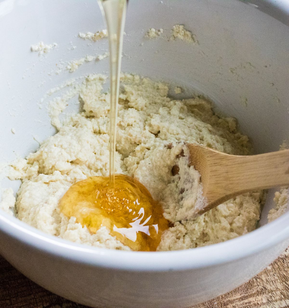 honey being poured into cornbread mixture in a white bowl with a wooden spoon in it