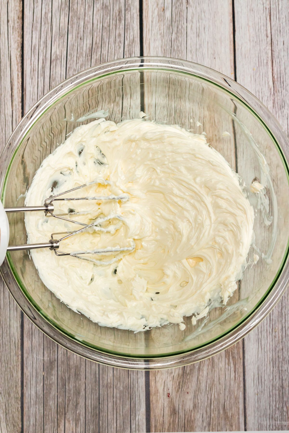 cream cheese and buttermilk being mixed in a clear bowl on a wood table