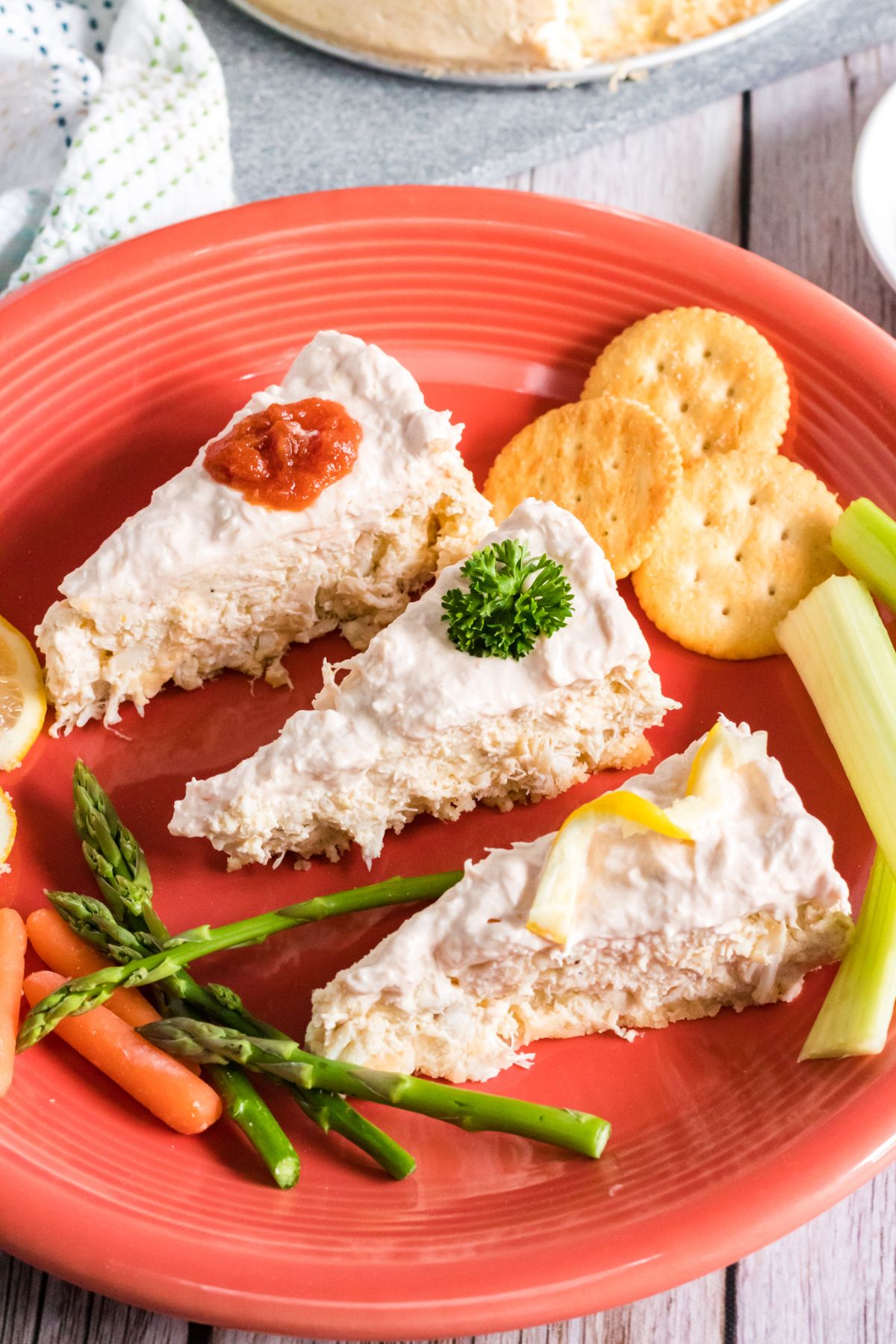 Instant Pot Crab Cheesecake sliced on a red  plate with vegetables, sliced lemon and crackers on the side. 