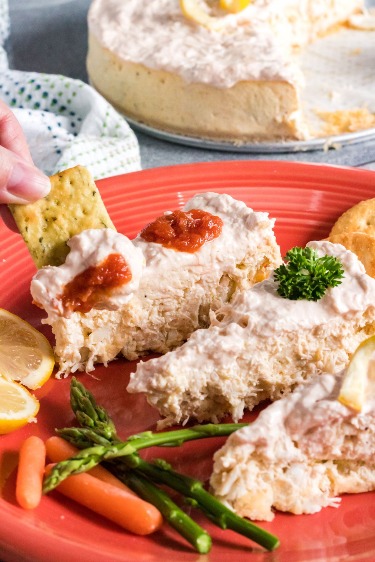 Instant Pot Crab Cheesecake sliced on a red plate with vegetables, sliced lemon and crackers on the side. 