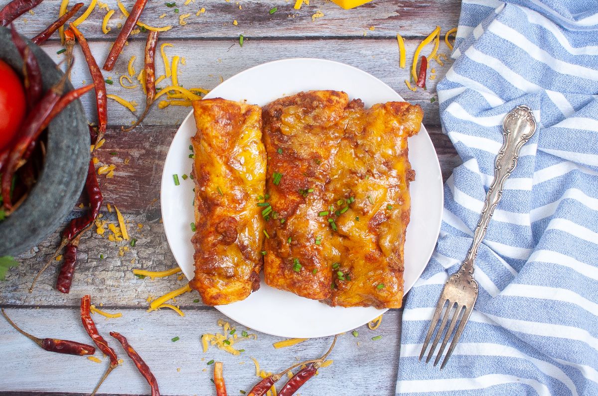 Air Fryer Enchiladas on a plate and garnished with chopped spring onion next to a fork on a blue and white striped cloth