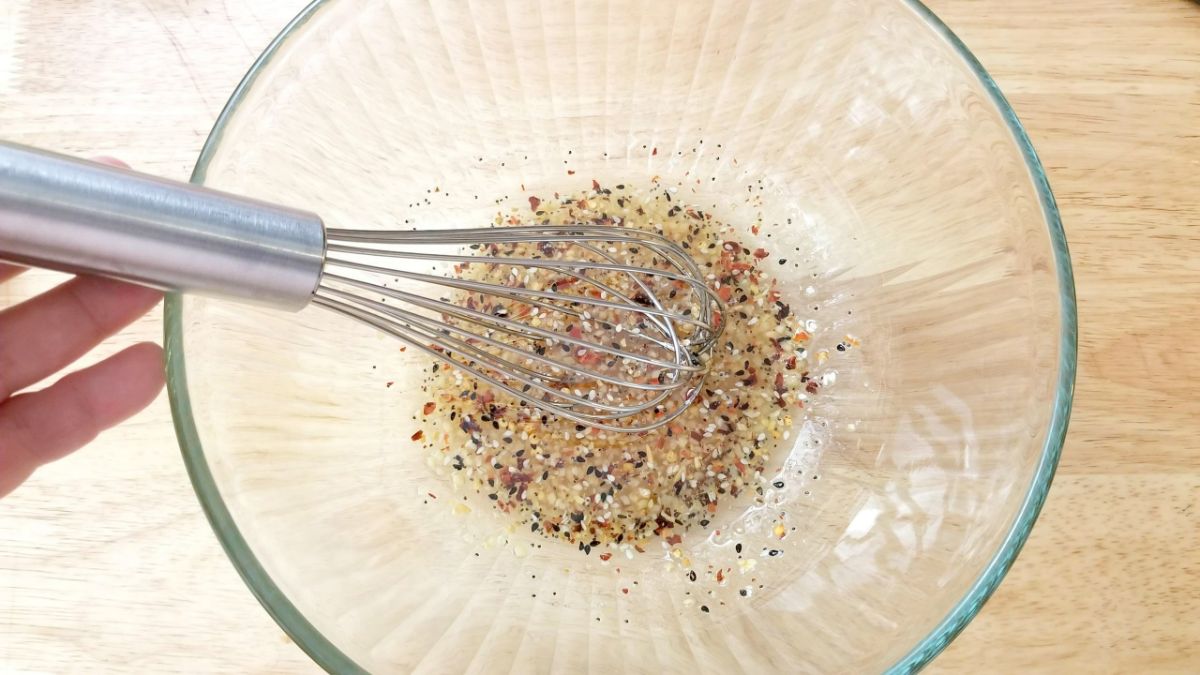 Mixture of olive oil, balsamic vinegar, garlic, salt and pepper, and red pepper flakes in a glass bowl with a wire whisk
