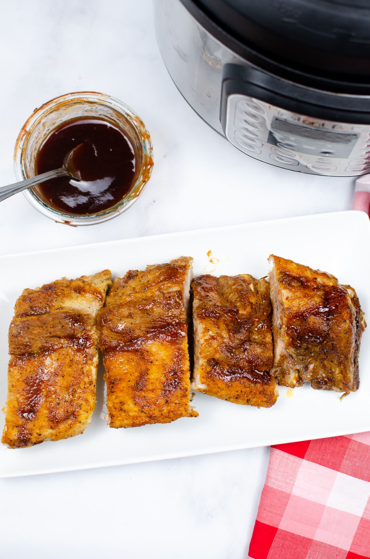 overhead view of Pressure Cooker Ribs on a white plate next to an instant pot and sauce in a glass bowl with a spoon in it