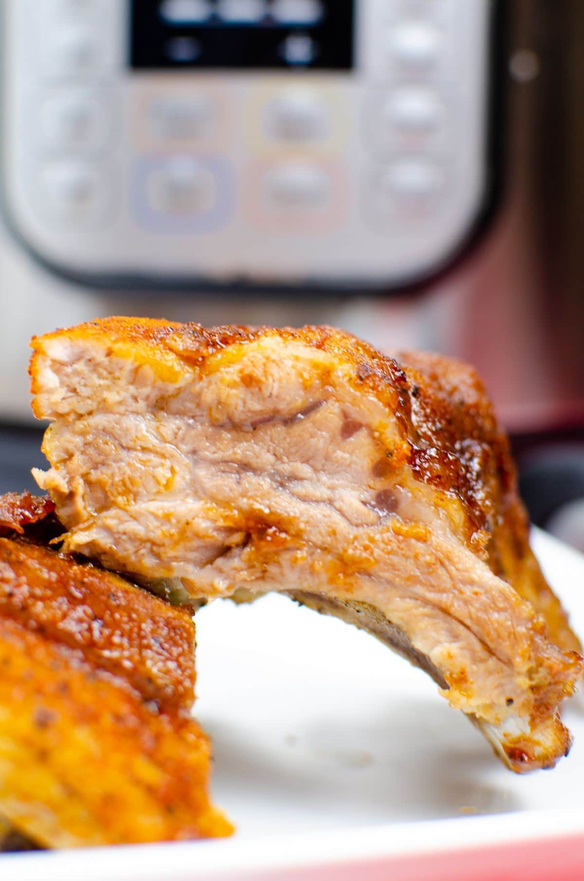 a closeup of Pressure Cooker Ribs on a white plate with an instant pot blurred in the background