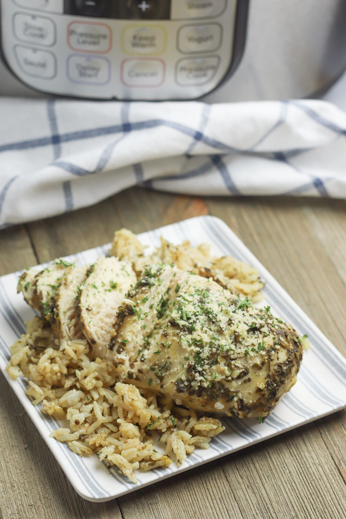 Instant Pot Chicken Breasts and Rice on a plate garnished with parmesan cheese and parsley with a blue and white cloth and an instant pot in the background