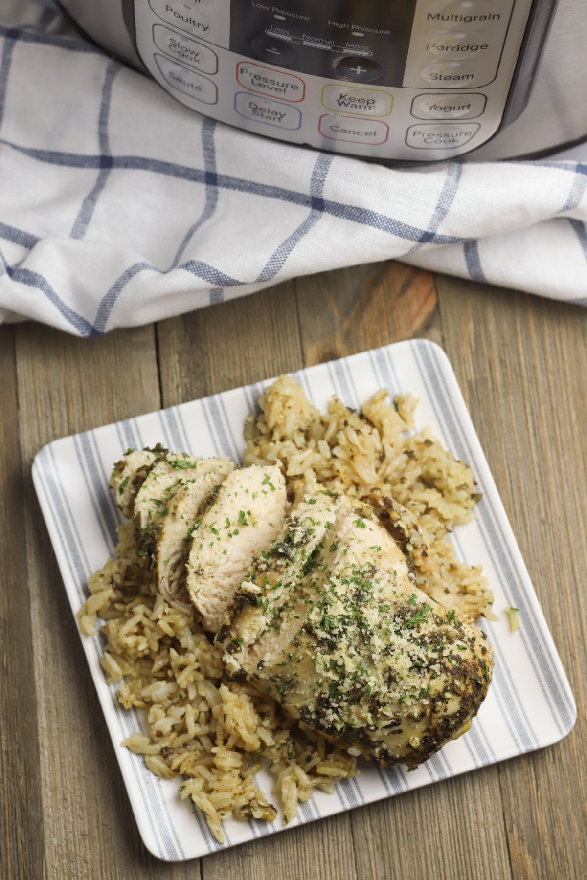 overhead view of Instant Pot Chicken Breasts and Rice on a plate garnished with parmesan cheese and parsley with a blue and white cloth and an instant pot in the background