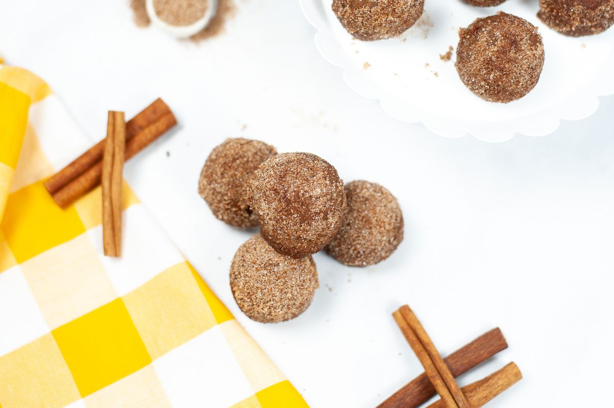 Instant Pot Churro Bites coated in cinnamon and sugar next to cinnamon sticks on a white plate on a yellow and white checkered cloth