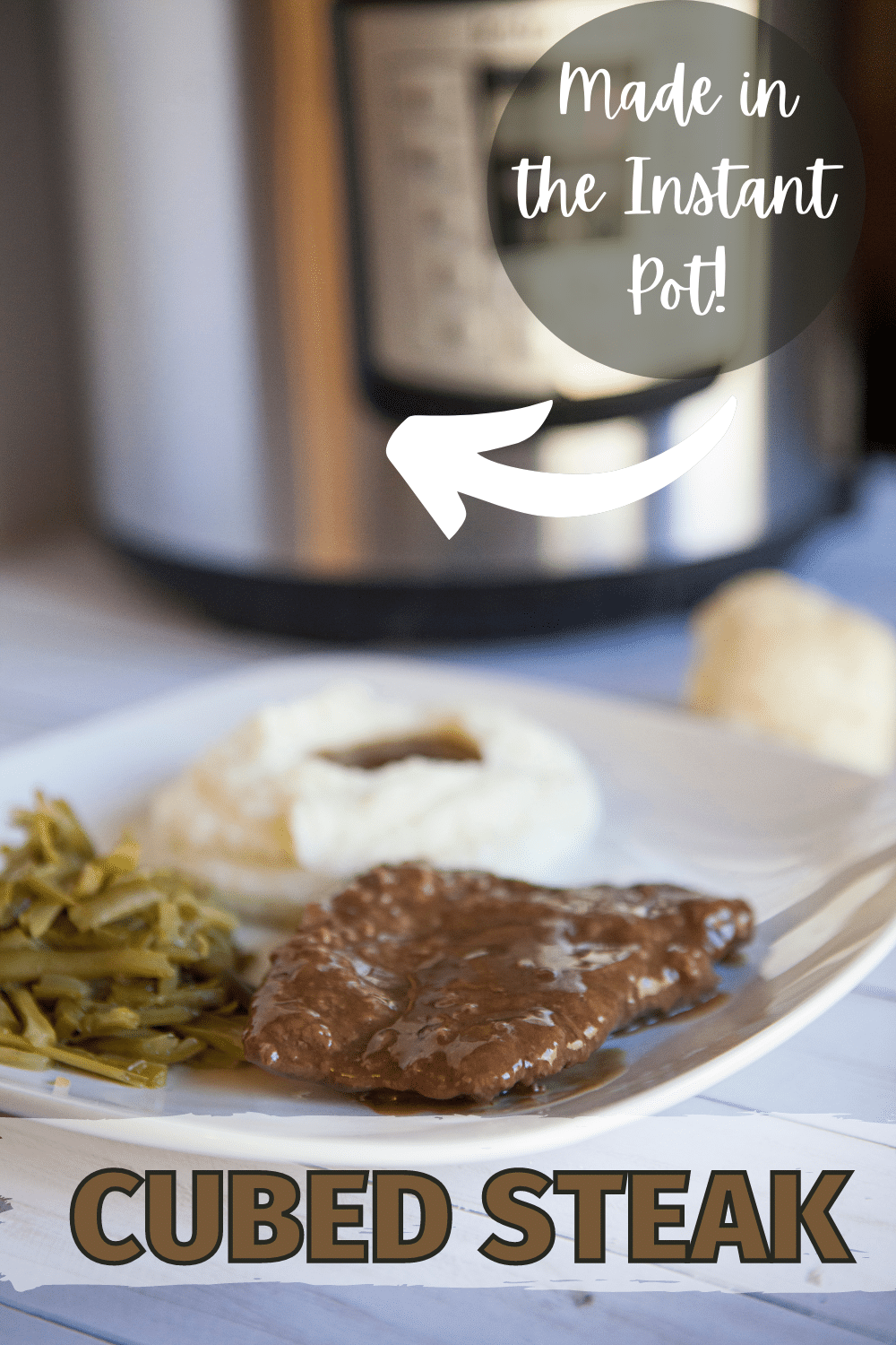 Instant Pot Cubed Steak on a white square plate with mashed potato and veggie on the side with an instant pot blurred in the background with title text reading Cubed Steak made in the instant pot