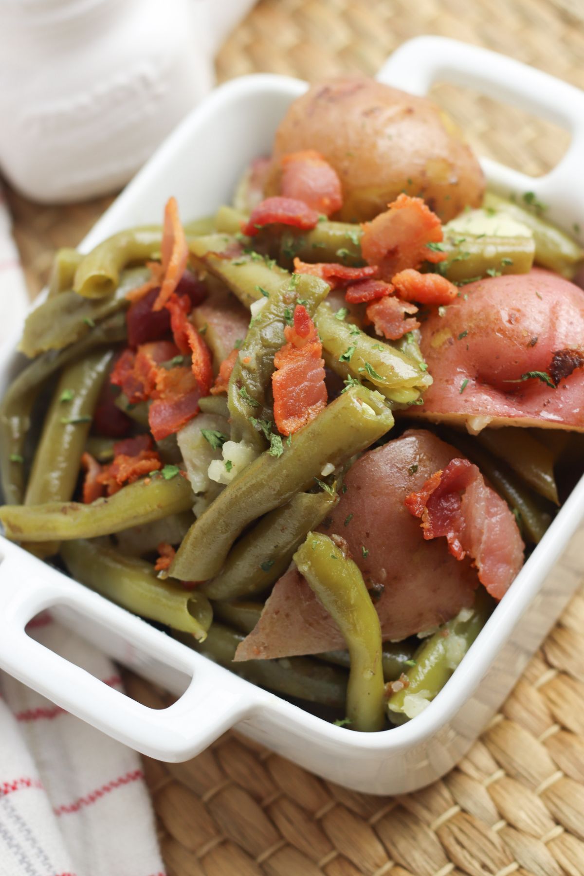 a closeup of Instant Pot Green Beans and Potatoes topped with bacon in a square white dish 