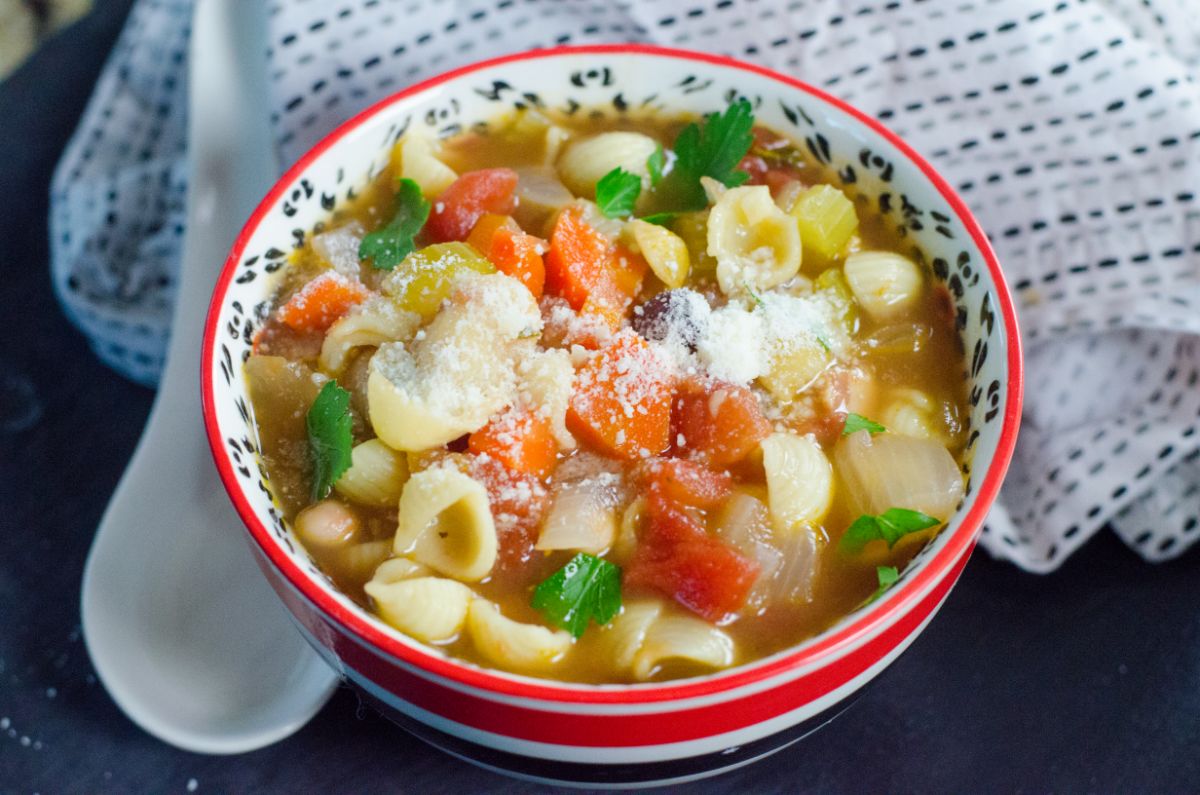 Instant Pot Pasta Fagioli in a bowl garnished with parsley leaves and parmesan cheese next to a cloth and a white spoon rest