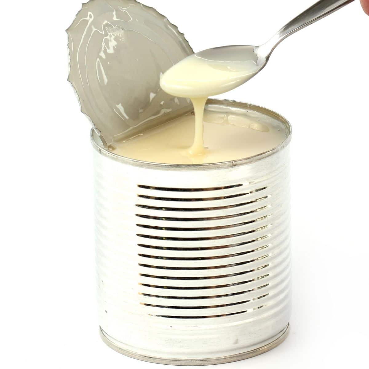 open can of sweetened condensed milk with spoon held above that appears to have just been dipped in the can