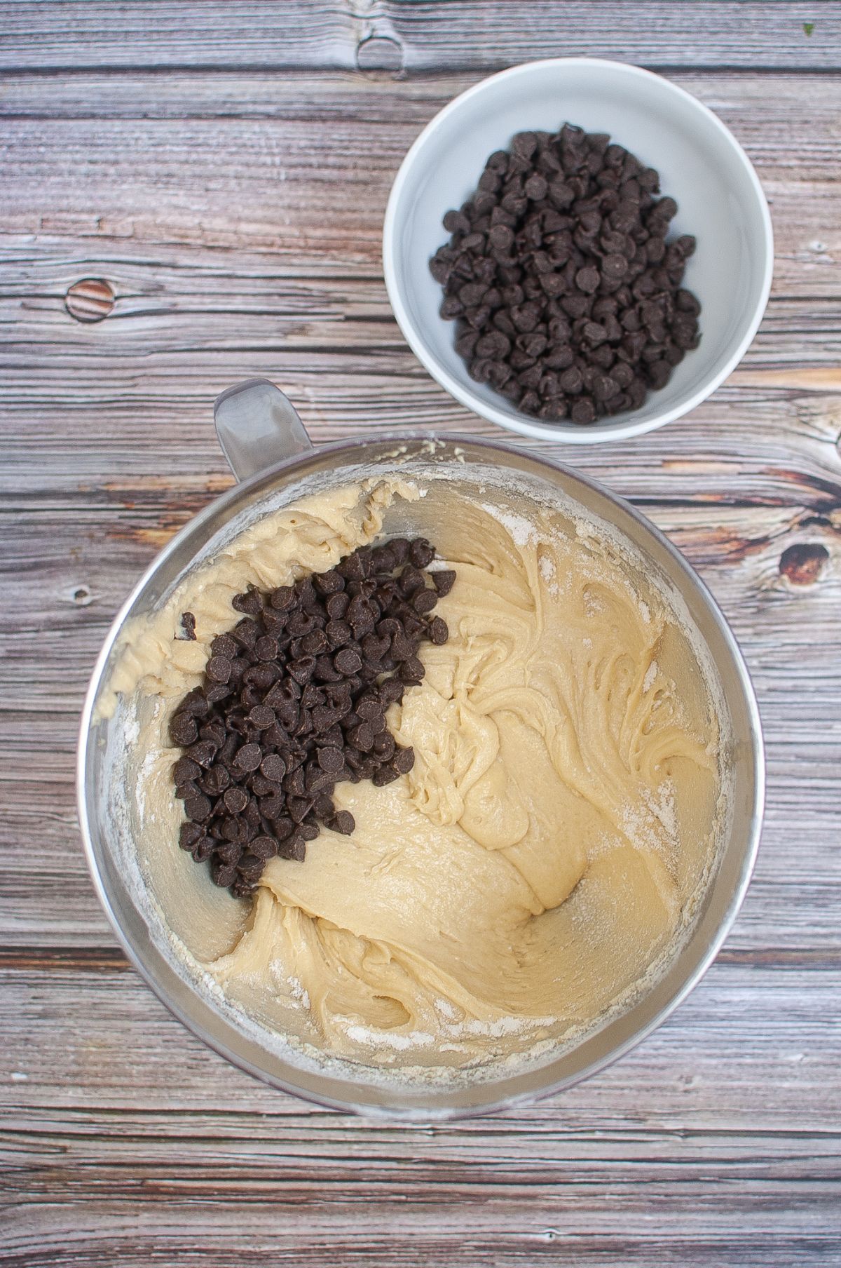 chocolate chips added to the muffin batter in a mixing bowl next to more chocolate chips in a white bowl