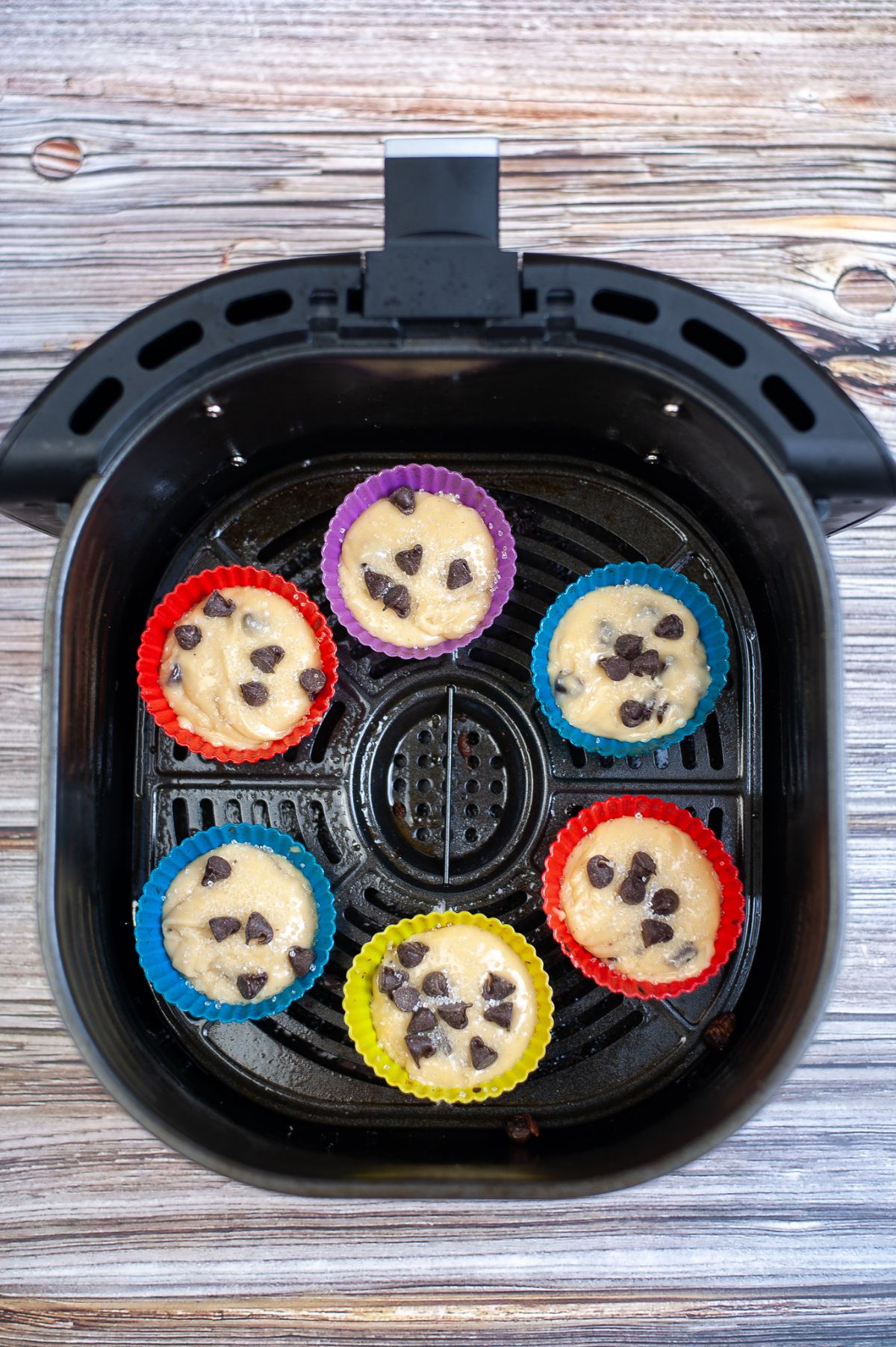 muffin batter in silicone molds  topped with chocolate chips and placed inside the air fryer
