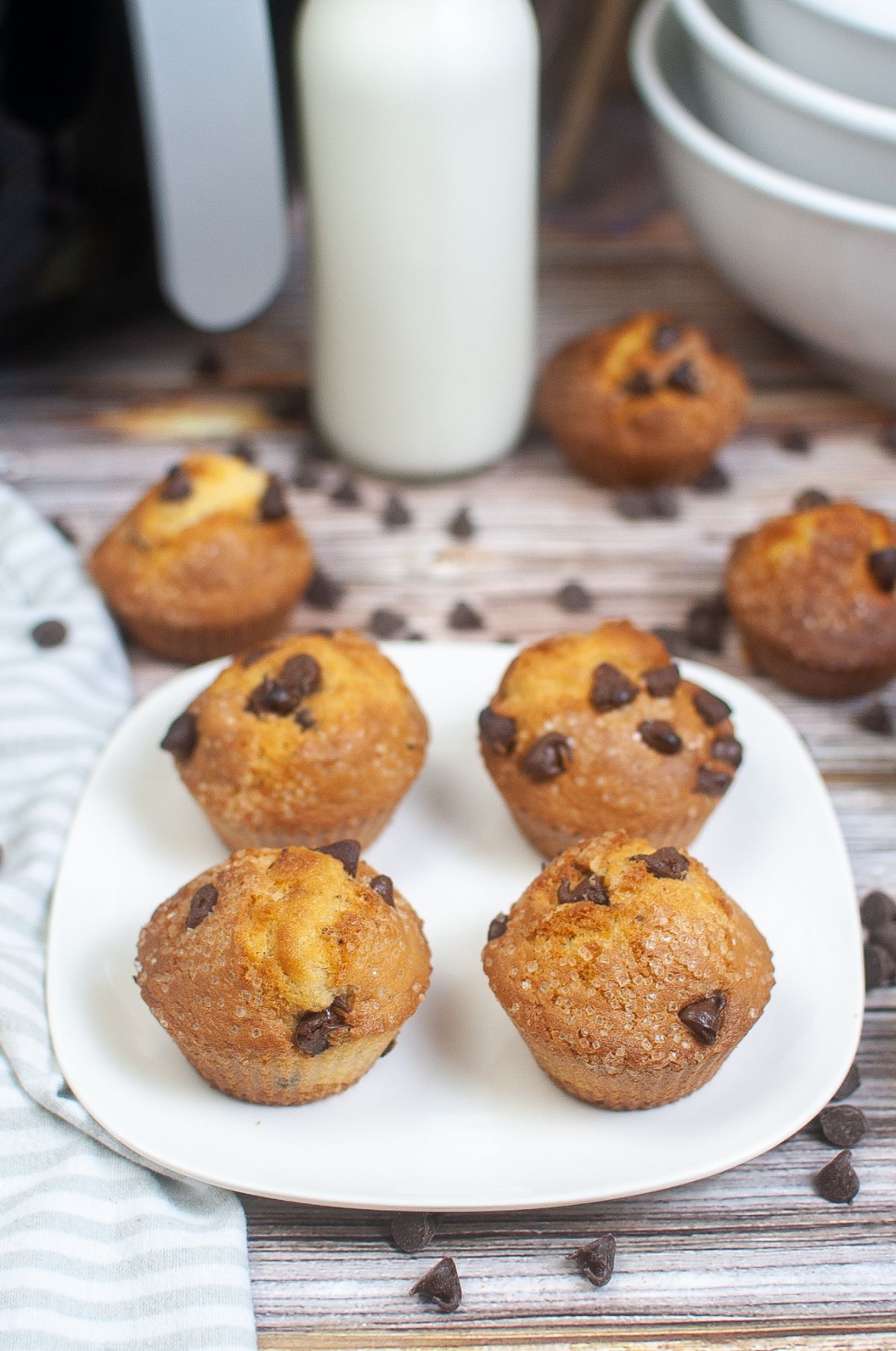 Air Fryer Chocolate Chip Muffins on a white plate with more muffins and chocolate chips in the background