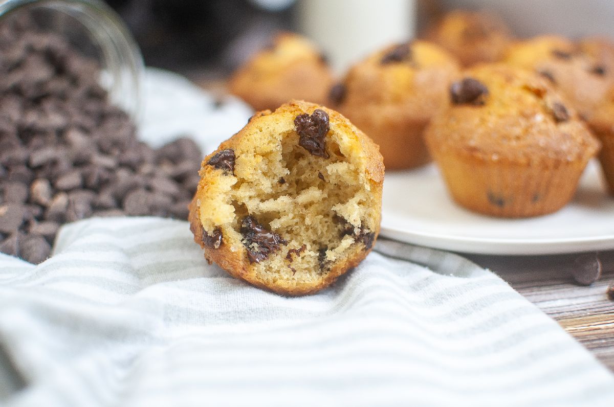 half of a  Chocolate Chip Muffin with more muffins and chocolate chips in the background