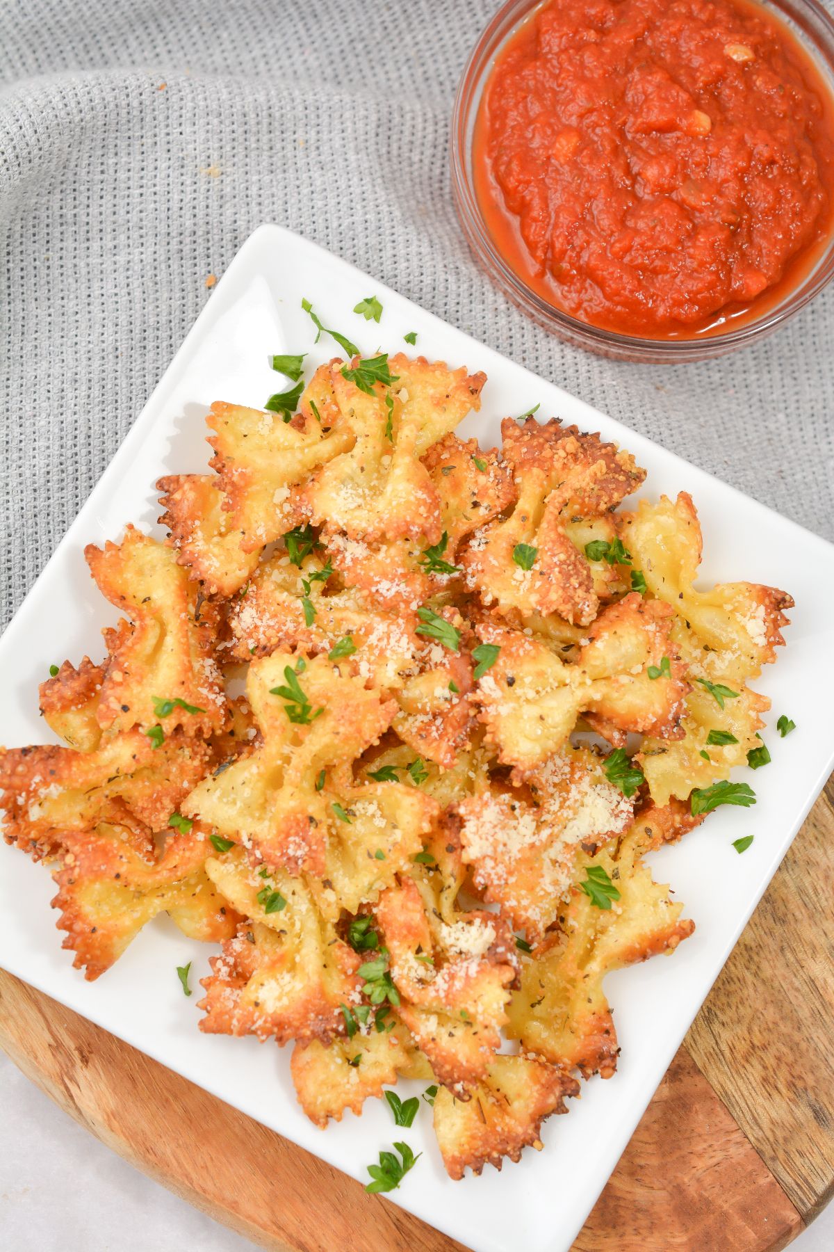 air fryer pasta chips on a white plate next to pasta sauce in a glass bowl