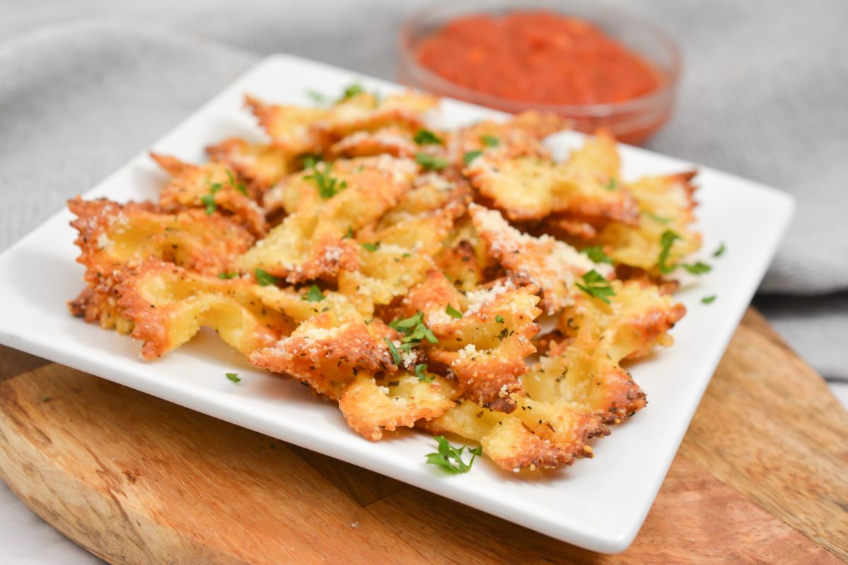 air fryer pasta chips on a white plate next to pasta sauce in a glass bowl