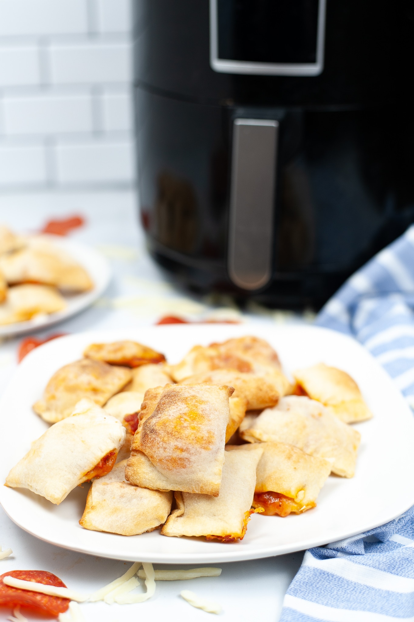Air Fryer Pizza Rolls on a white plate with more pizza rolls and an air fryer blurred in the background