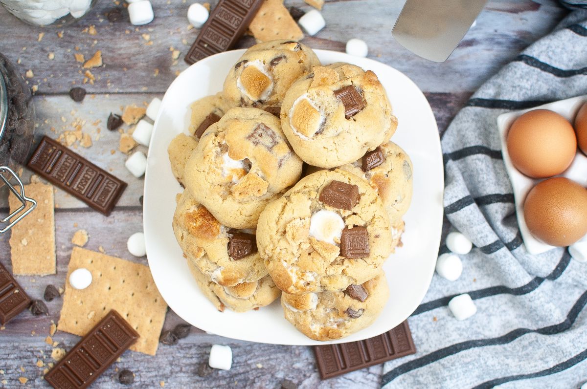 overhead view of a stack of cookies made from an Air Fryer Smores Cookie Recipe on a plate surrounded by graham crackers, chocolate bars, chocolate chips and marshmallows