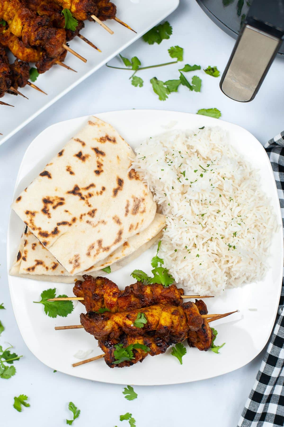 Air Fryer Tandoori Chicken on a plate with Naan bread and basmati rice garnished with parsley with more chicken on a white platter and an air fryer in the background