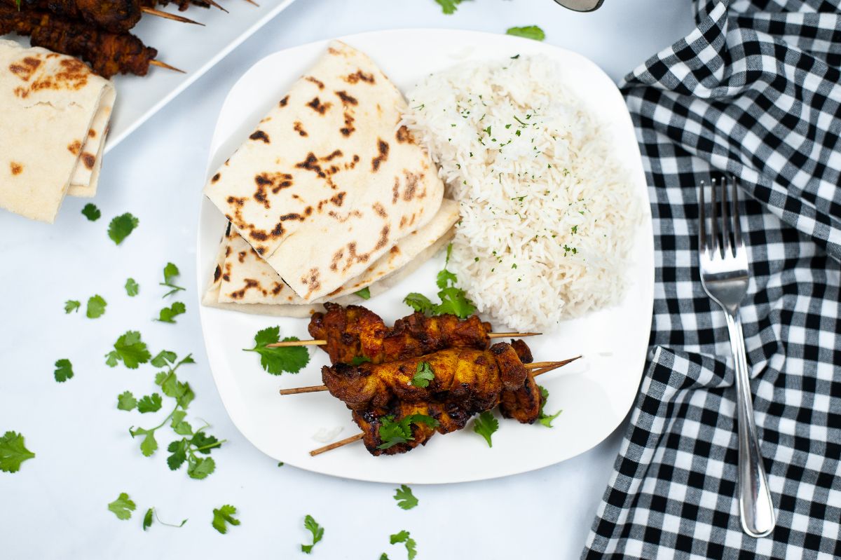 Air Fryer Tandoori Chicken on a plate with Naan bread and basmati rice garnished with celery leaves next to a fork on a black and white checkered cloth
