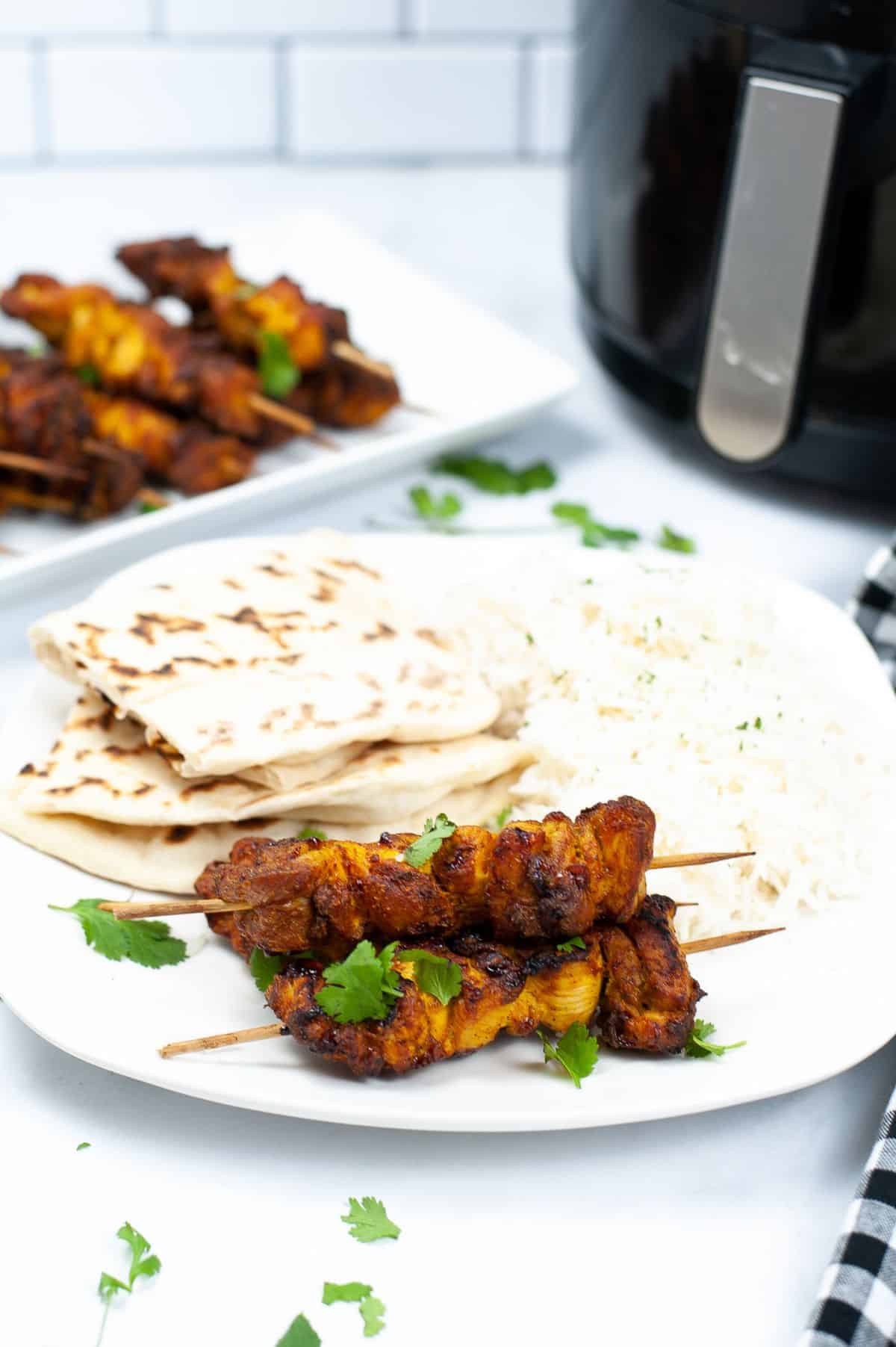 Air Fryer Tandoori Chicken on a plate with Naan bread and basmati rice garnished with parsley with more chicken on a white platter and an air fryer in the background