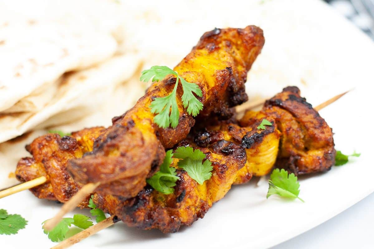 a closeup of Air Fryer Tandoori Chicken on a plate with Naan bread and basmati rice garnished with celery leaves