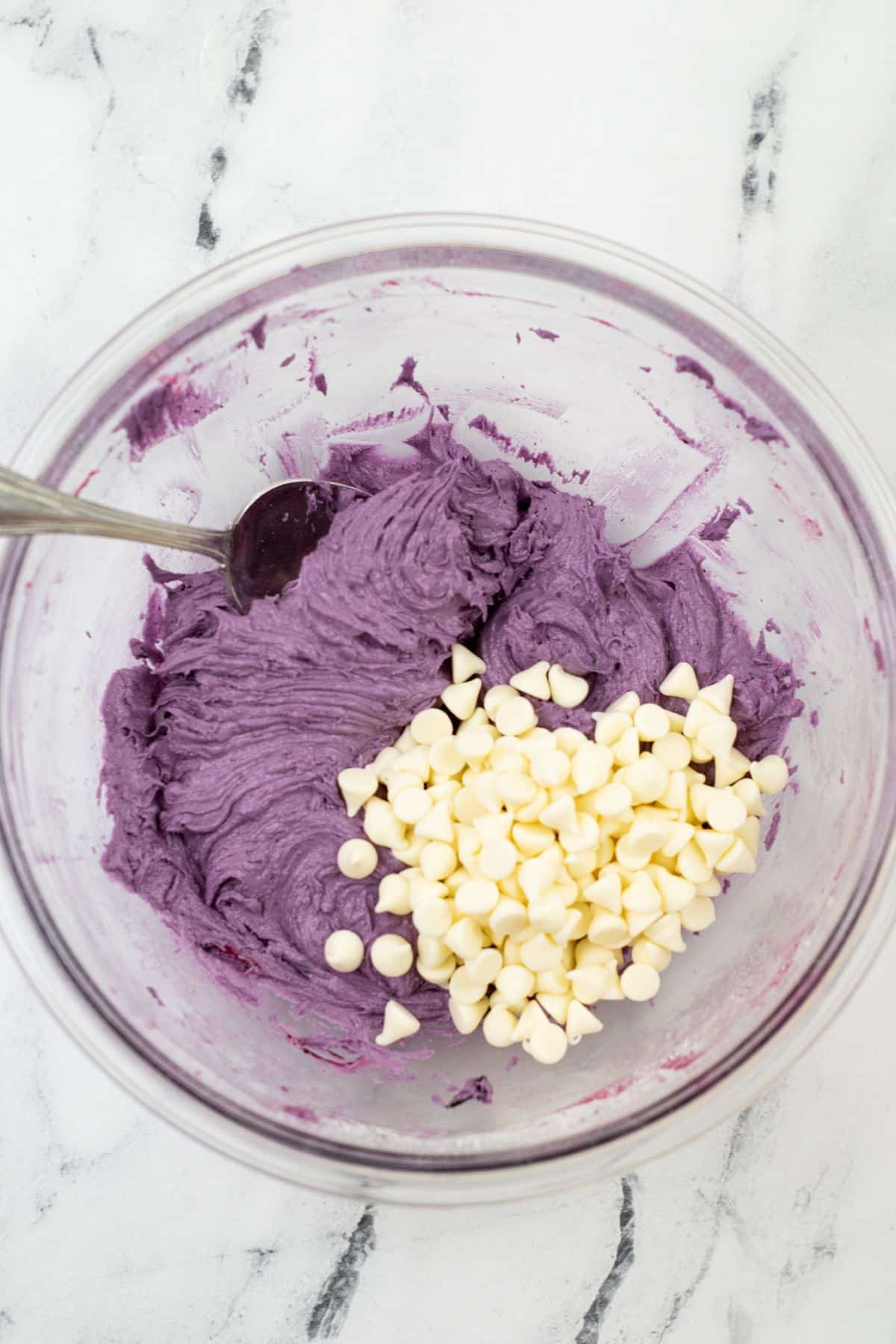 white chocolate chips being folded into the blueberry mixture in a glass bowl with a spoon