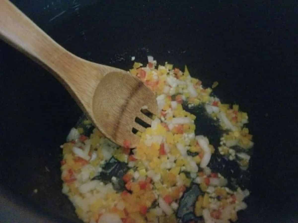 onions and bell peppers being cooked and stirred with a wooden spoon in the instant pot
