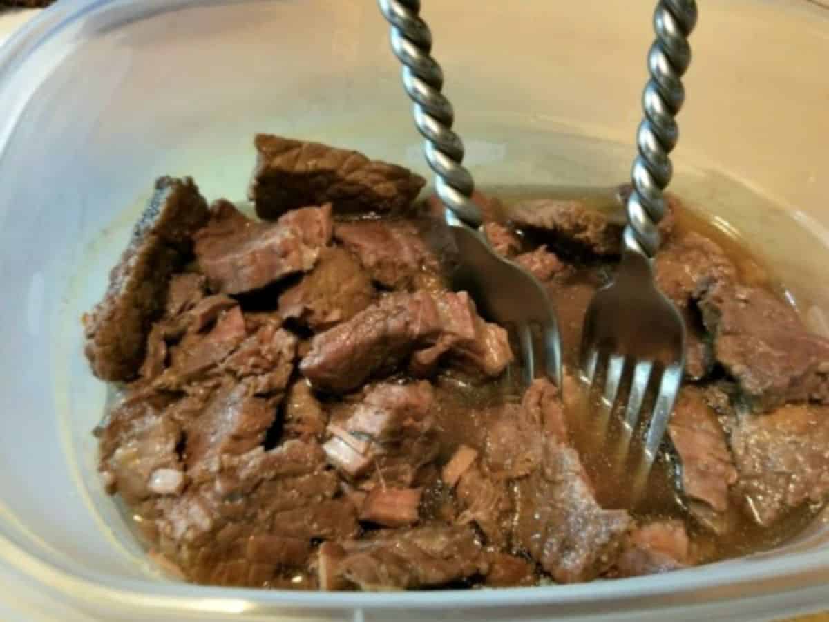 2 forks being used to shred the beef in a plastic container