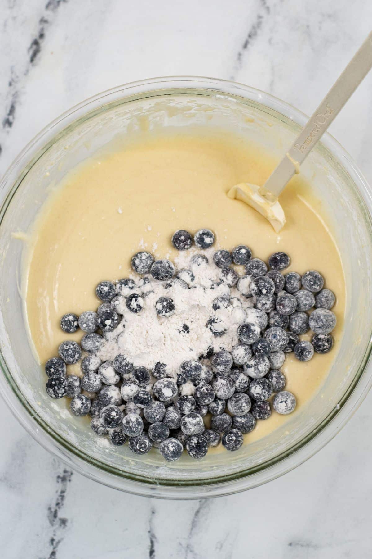 Batter and blueberries coated with flour in a bowl with a spatula in it