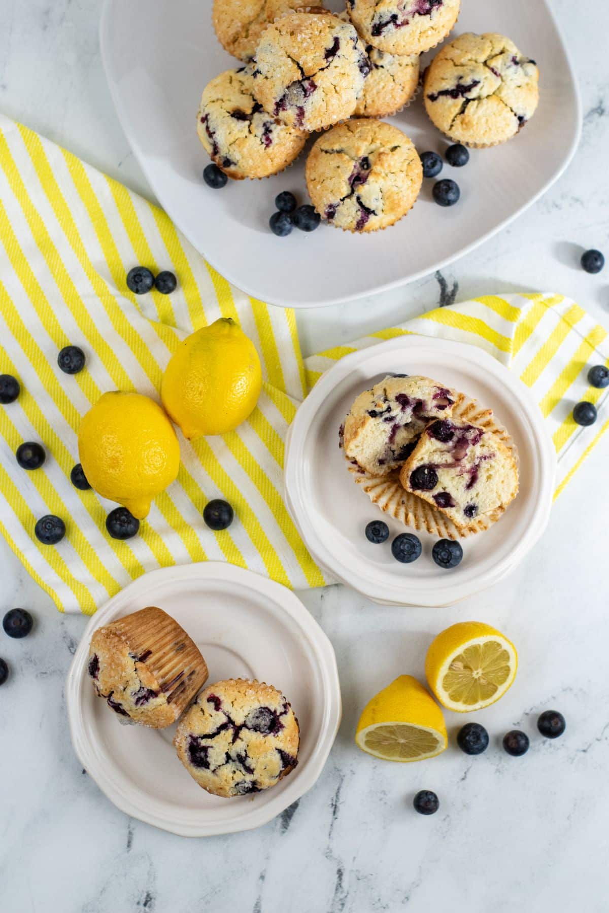 overhead view of Lemon Blueberry Muffins With Sour Cream on several plates surrounded by blueberries and lemons