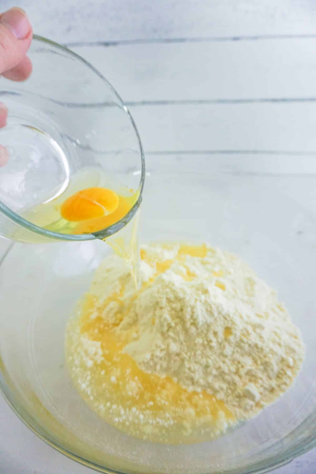 eggs being poured from a glass bowl into cake mix in another glass bowl