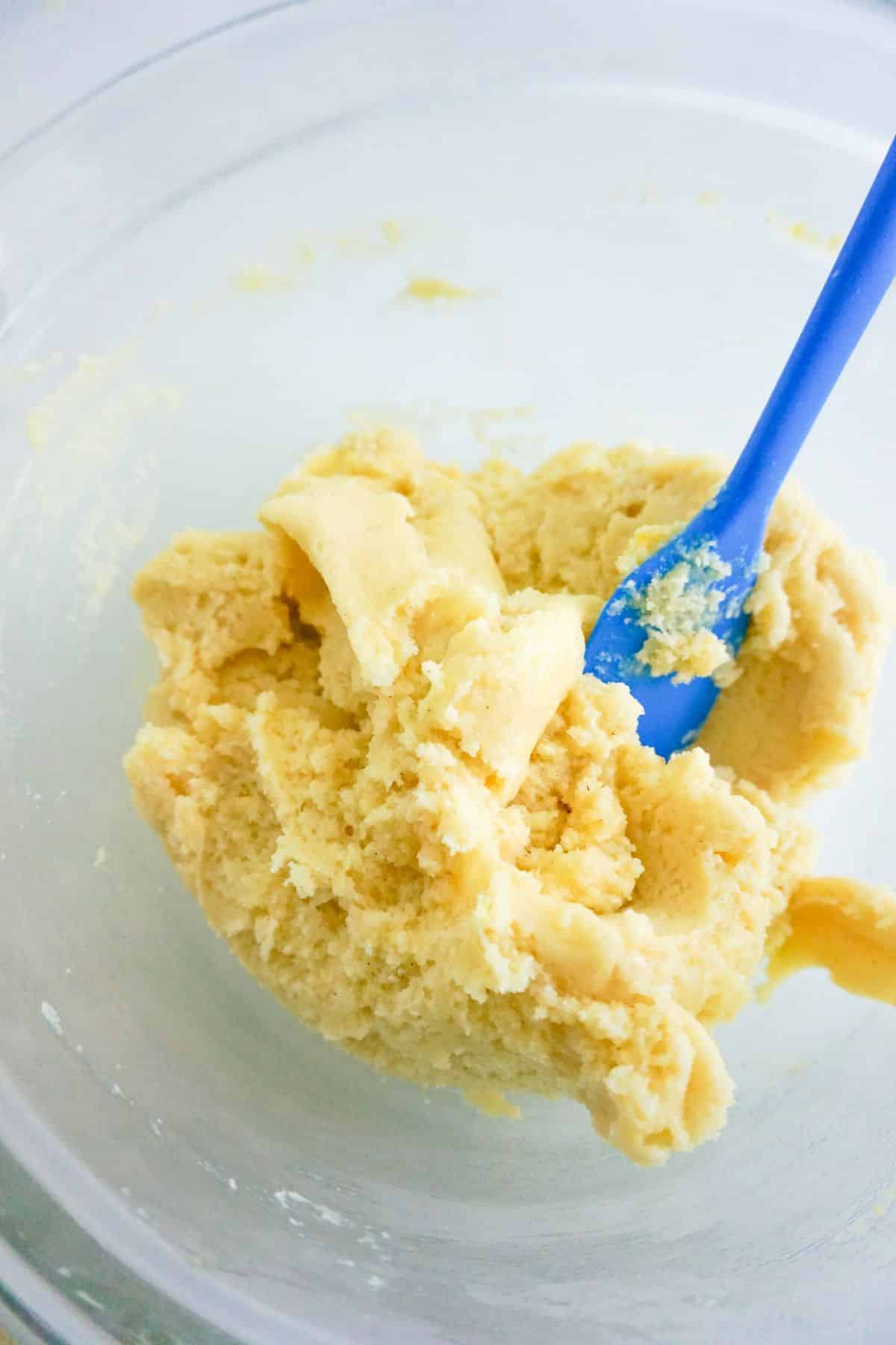 Chilled cookie dough and a blue spatula in a glass bowl