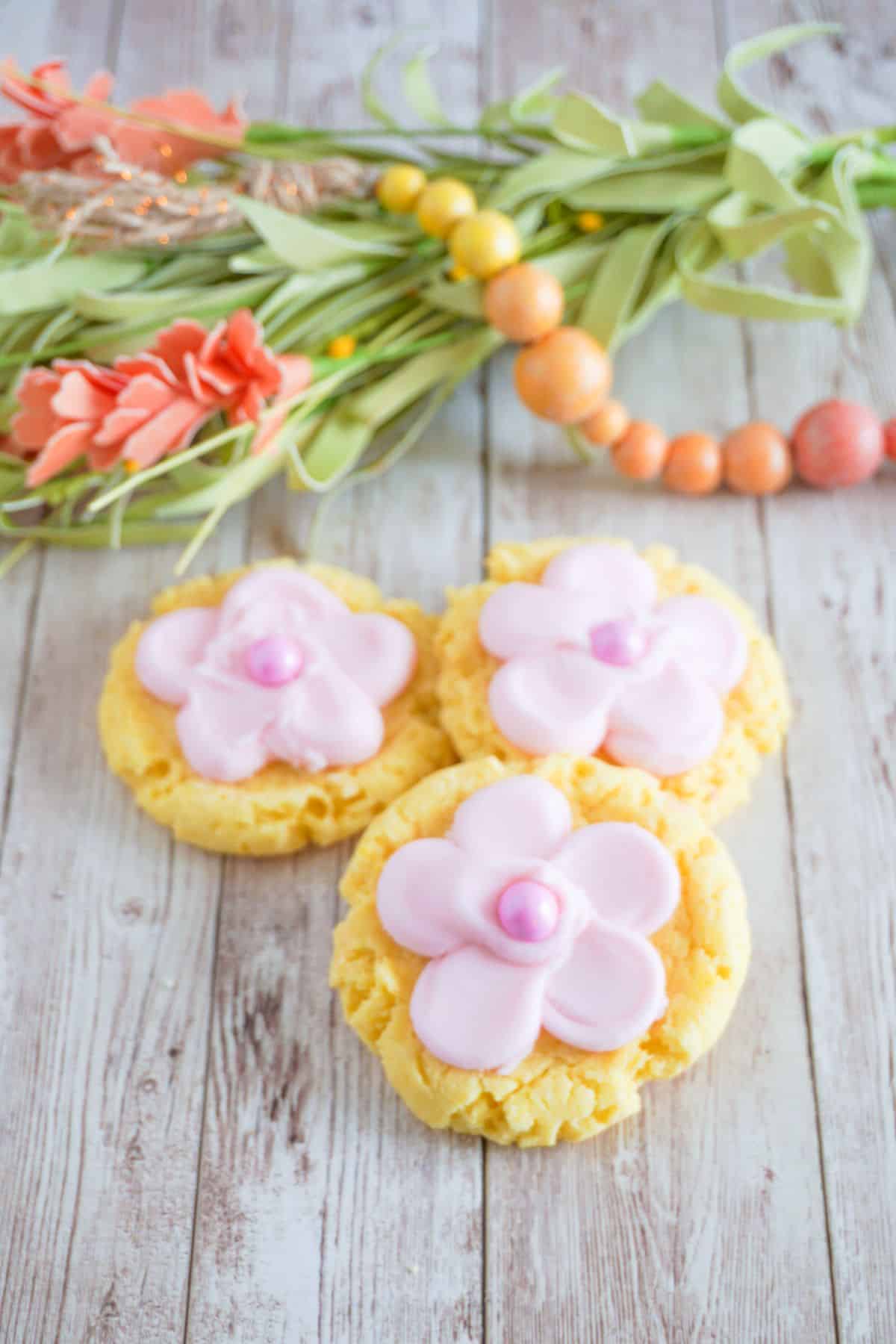 Lemon Cake Mix Cookies With Frosting made to look like a flower next to some greenery and beads
