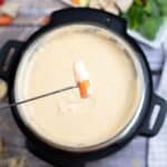 A fork dipping a vegetable piece into a melting pot of Swiss cheese fondue.