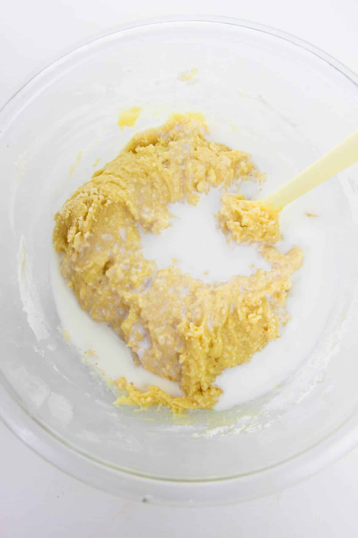 flour mixture and milk in a glass bowl being combined using a spatula