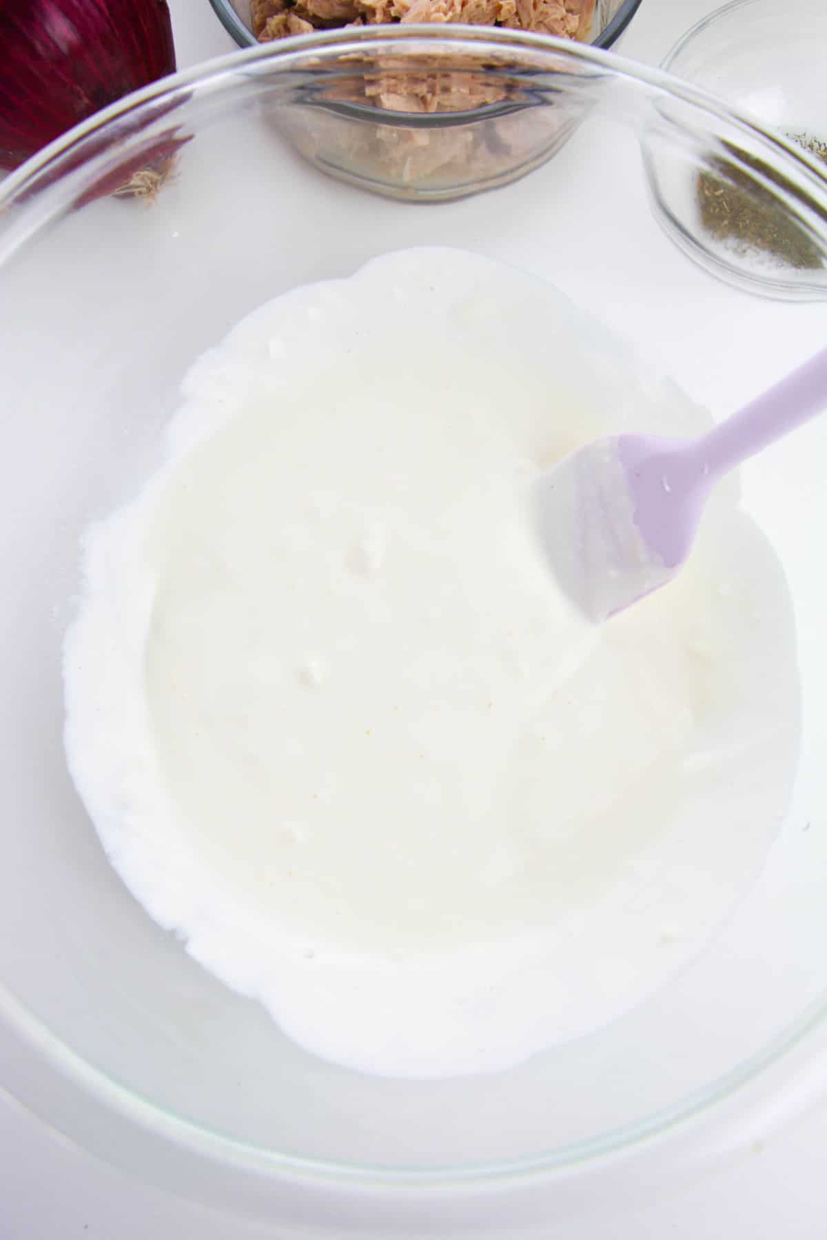 mayo, yogurt, and lemon juice in a glass bowl with a spatula in it
