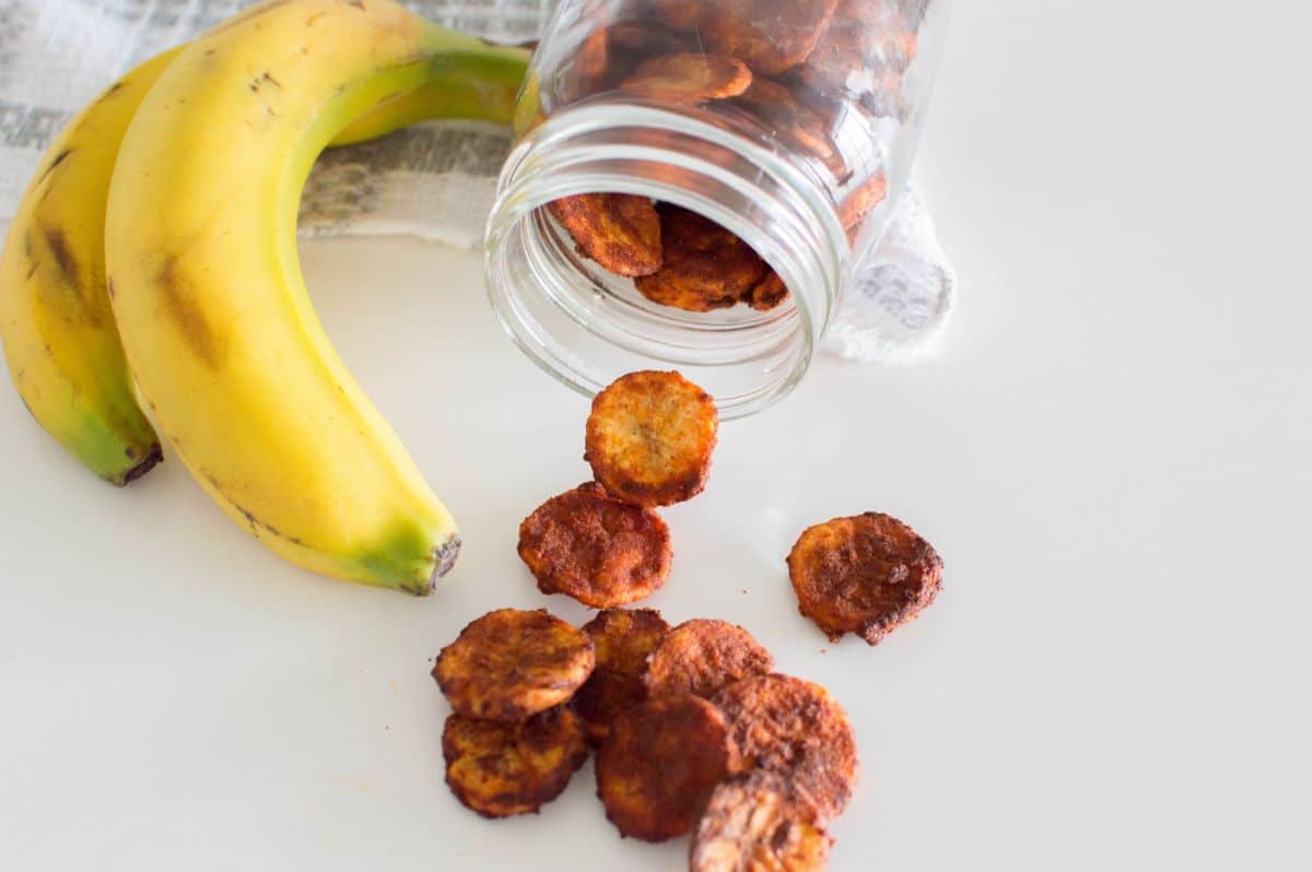 Air Fryer Banana Chips in a jar and on a table  with bananas on the side