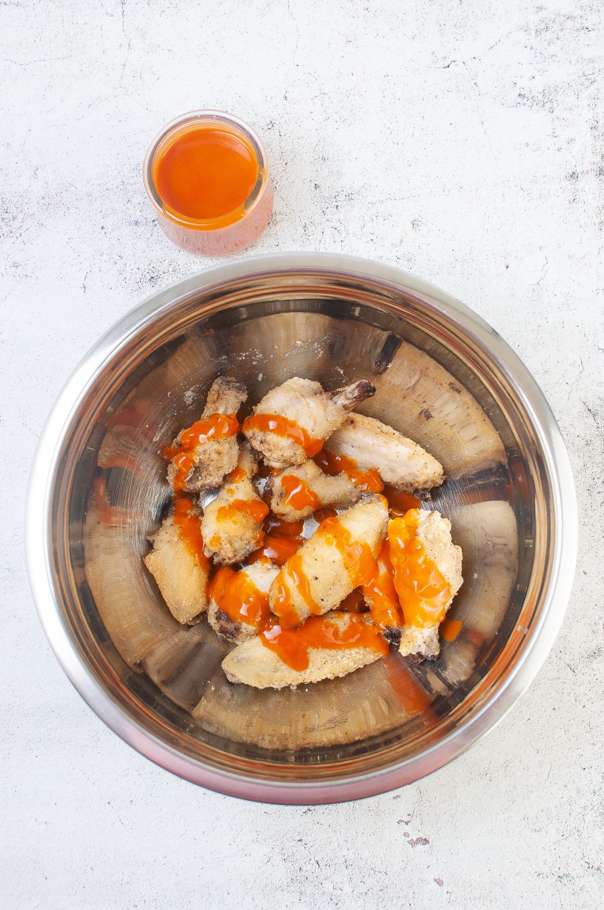 Cooked chicken wings in a mixing bowl with Buffalo sauce.