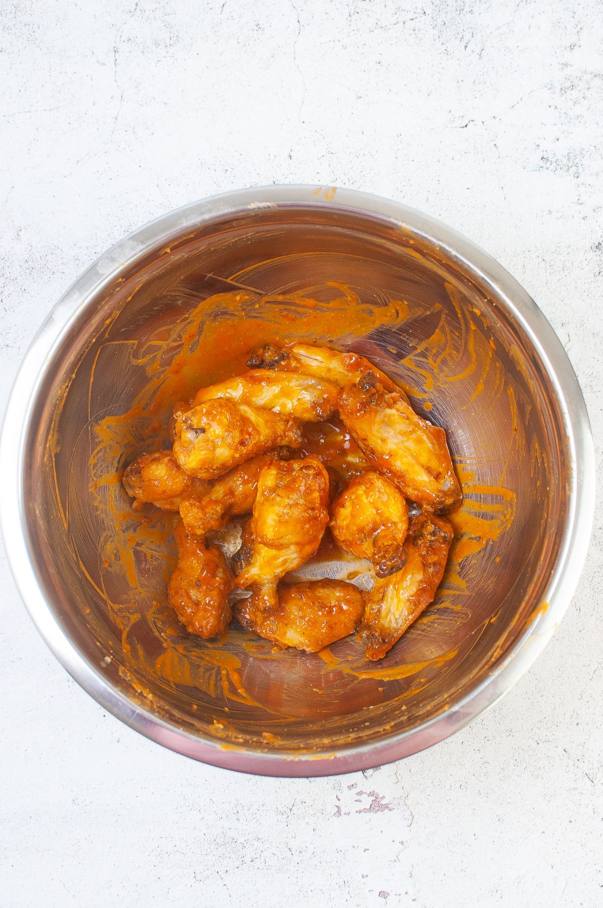 Cooked chicken wings in a mixing bowl tossed with remaining Buffalo sauce.