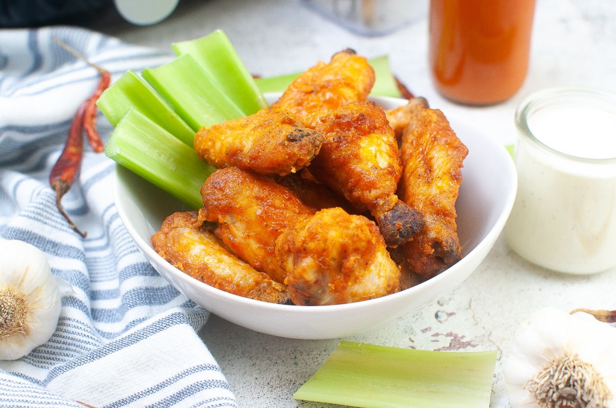 Air Fryer Buffalo Wings in a large bowl next to celery stalks, garlic clove, and sauce