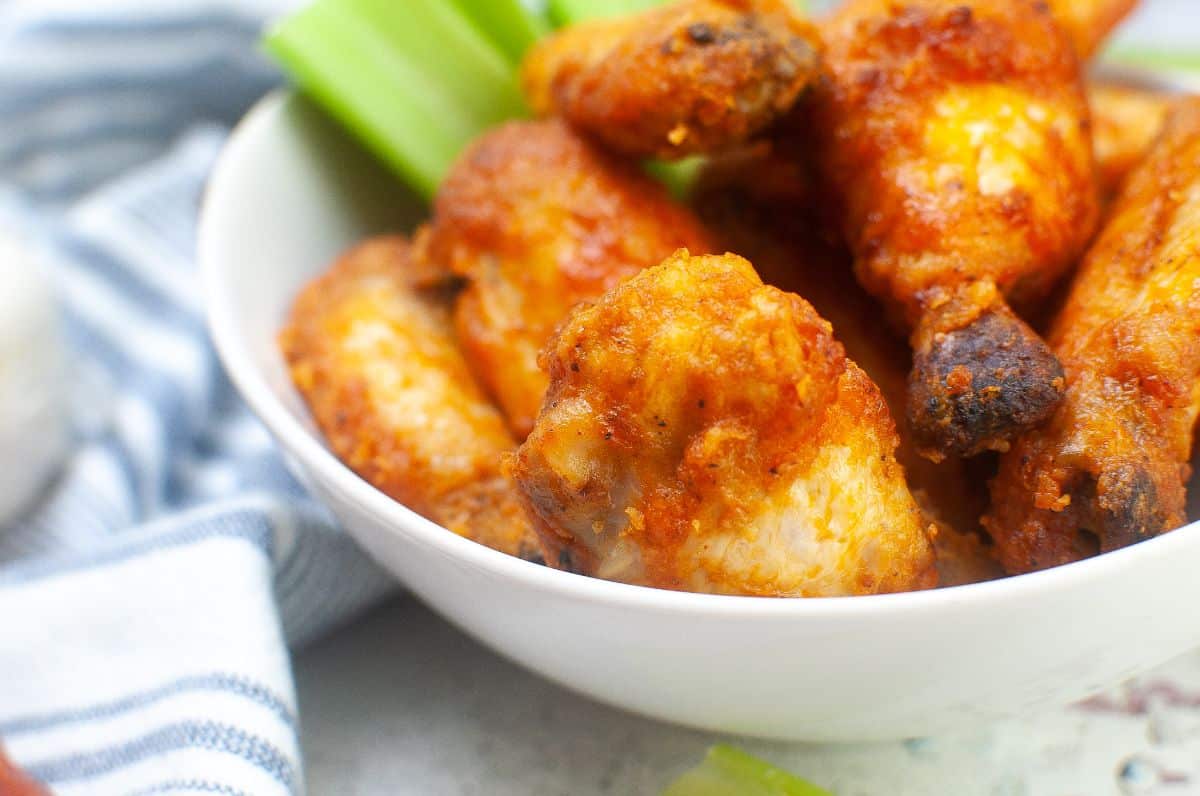 a closeup of Air Fryer Buffalo Wings in a large bowl next to celery stalks