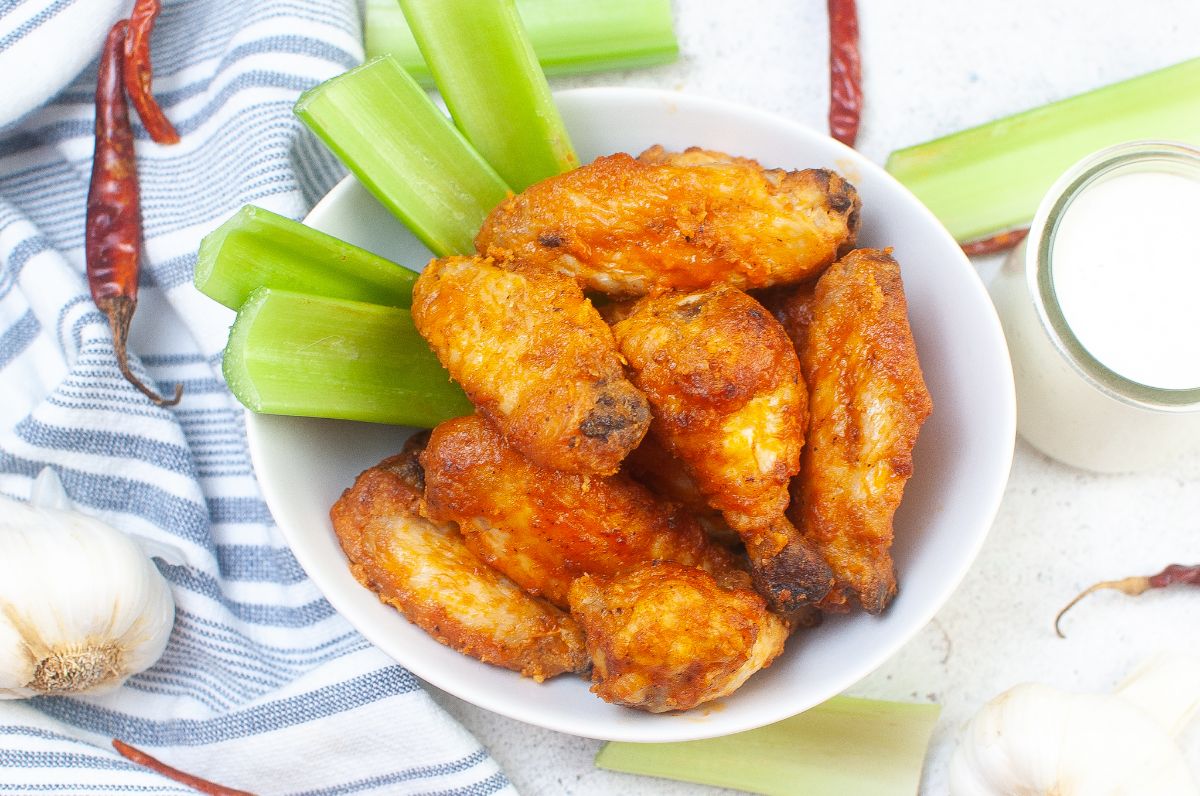 Air Fryer Buffalo Wings in a large bowl next to celery stalks, garlic clove, and sauce