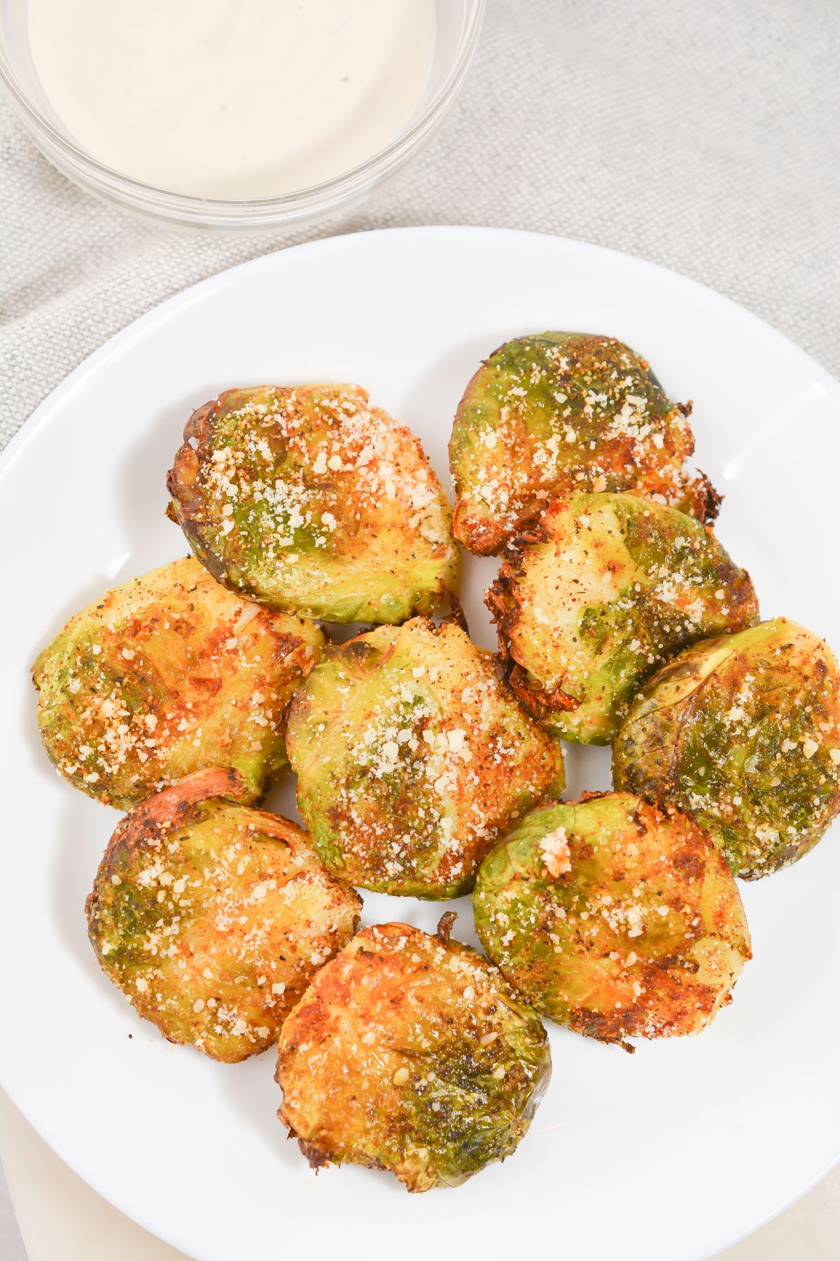 a closeup of Air Fryer Keto Brussel Sprouts on a white plate and with dip on the side in a glass bowl