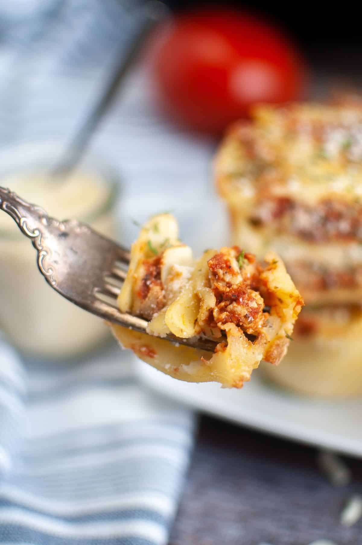 closeup of lasagna on a fork with more lasagna cups blurred in the background